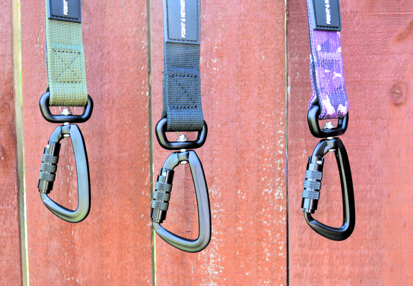 Three dog leashes with carabiners hanging on a wooden surface