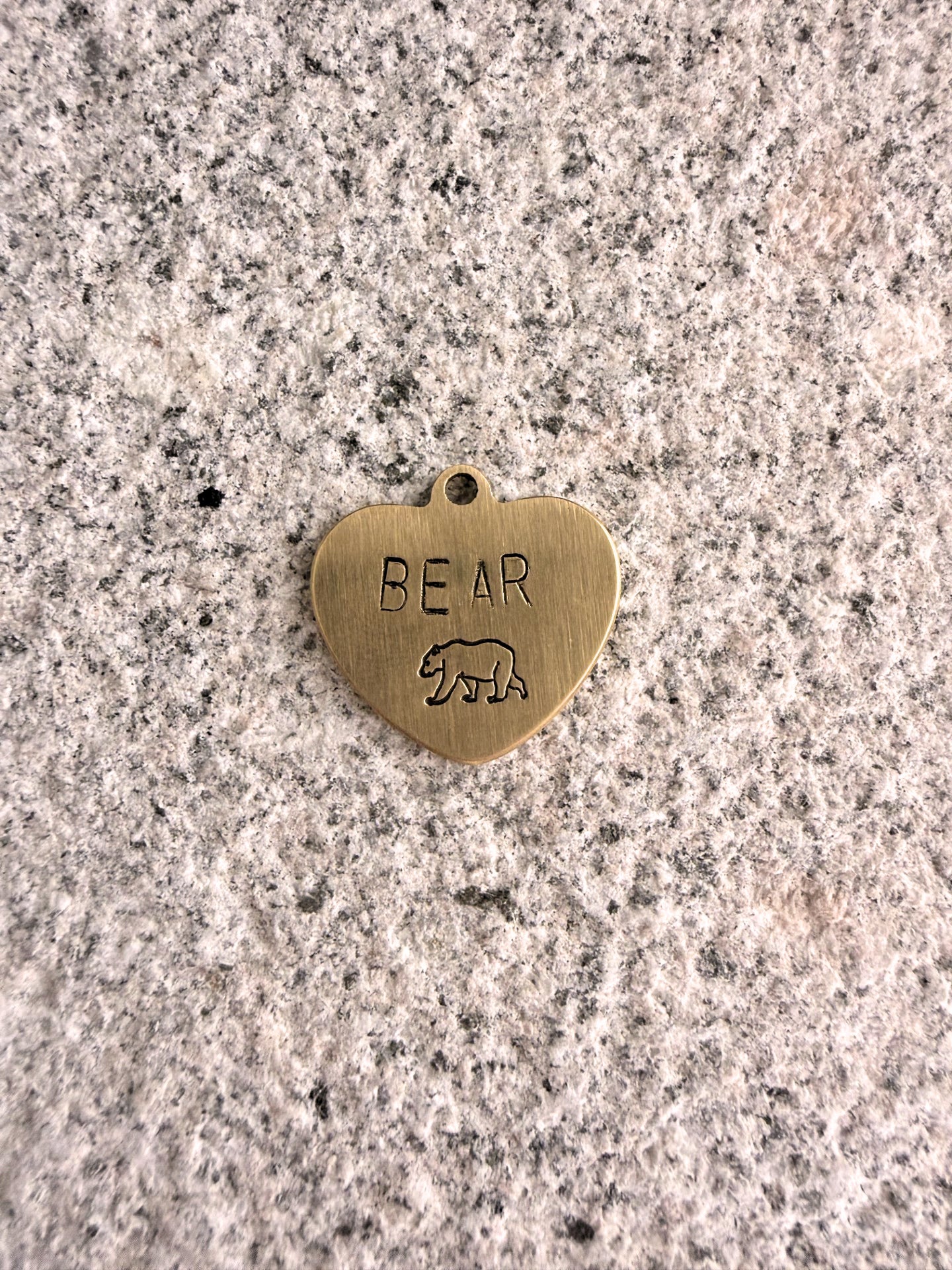 Heart-shaped brass pendant with 'BEAR' engraving on a speckled surface