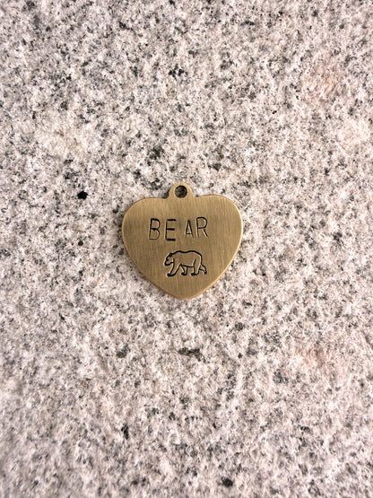 Heart-shaped brass pendant with 'BEAR' engraving on a speckled surface