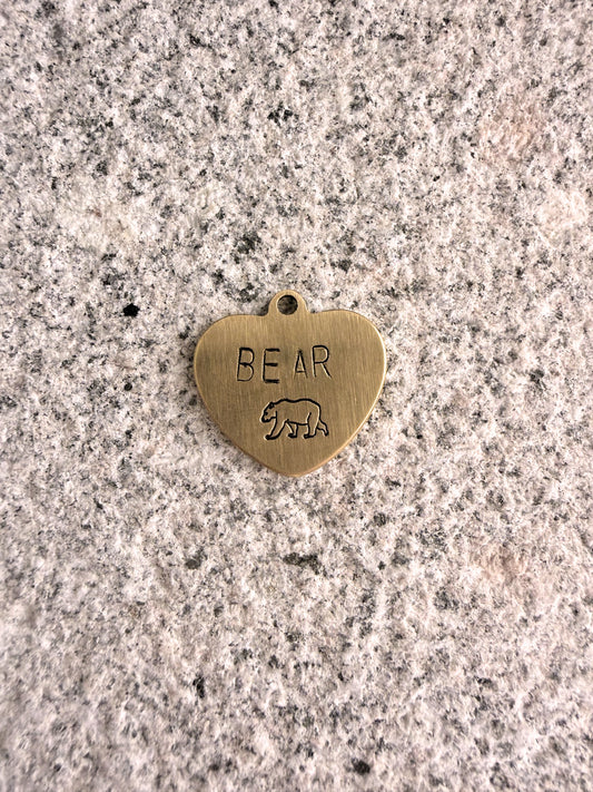 Heart-shaped brass pendant with 'BEAR' engraving on a speckled surface