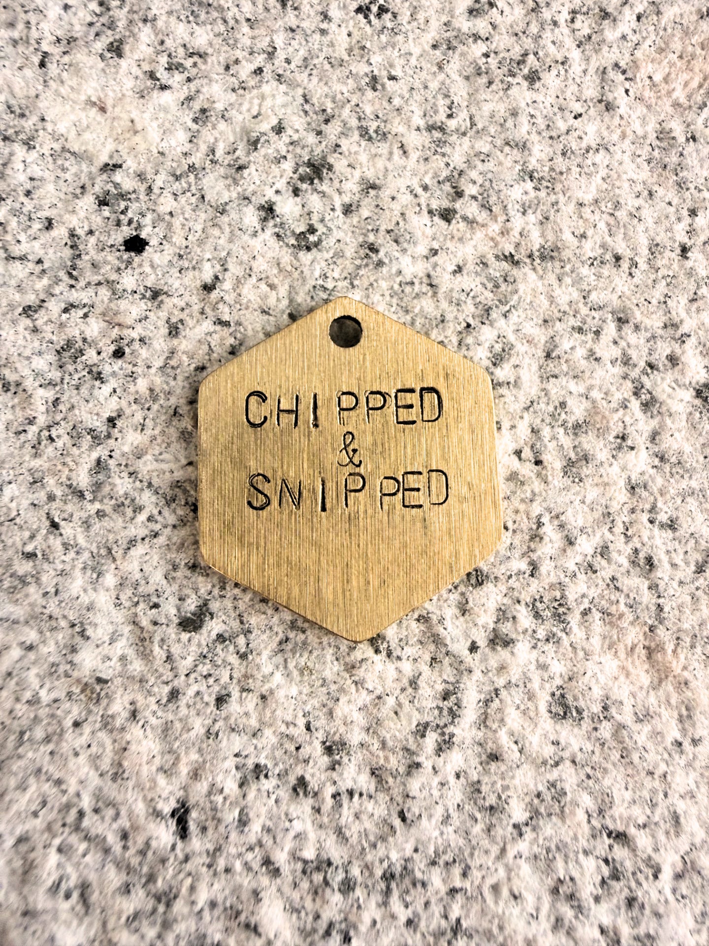 Hexagonal brass tag with 'CHIPPED & SNIPPED' text on a granite surface