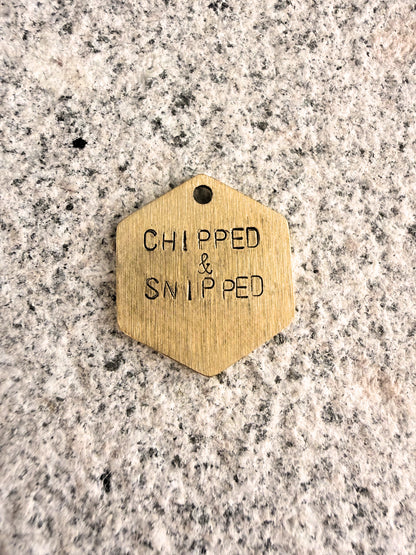 Hexagonal brass tag with 'CHIPPED & SNIPPED' text on a granite surface