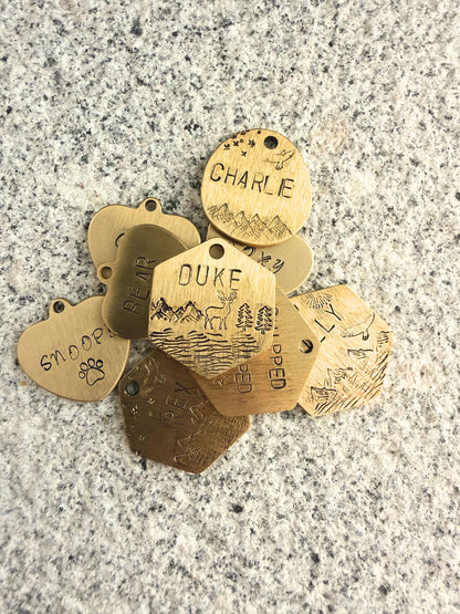 Collection of gold pet tags with engraved names on a gray surface