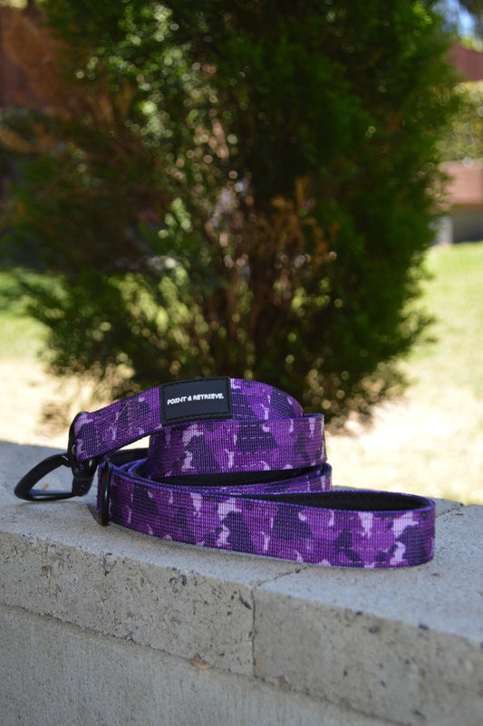 Purple camouflage dog leash on a stone ledge with blurred greenery in the background